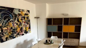 Un coin repas avec une table blanche, des chaises et un grand tableau abstrait accroché au mur.