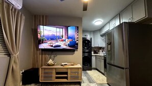 Une cuisine moderne dotée d’un four encastré, d’un réfrigérateur en acier inoxydable et d’un téléviseur fixé au mur qui diffuse des images d’un paysage urbain.