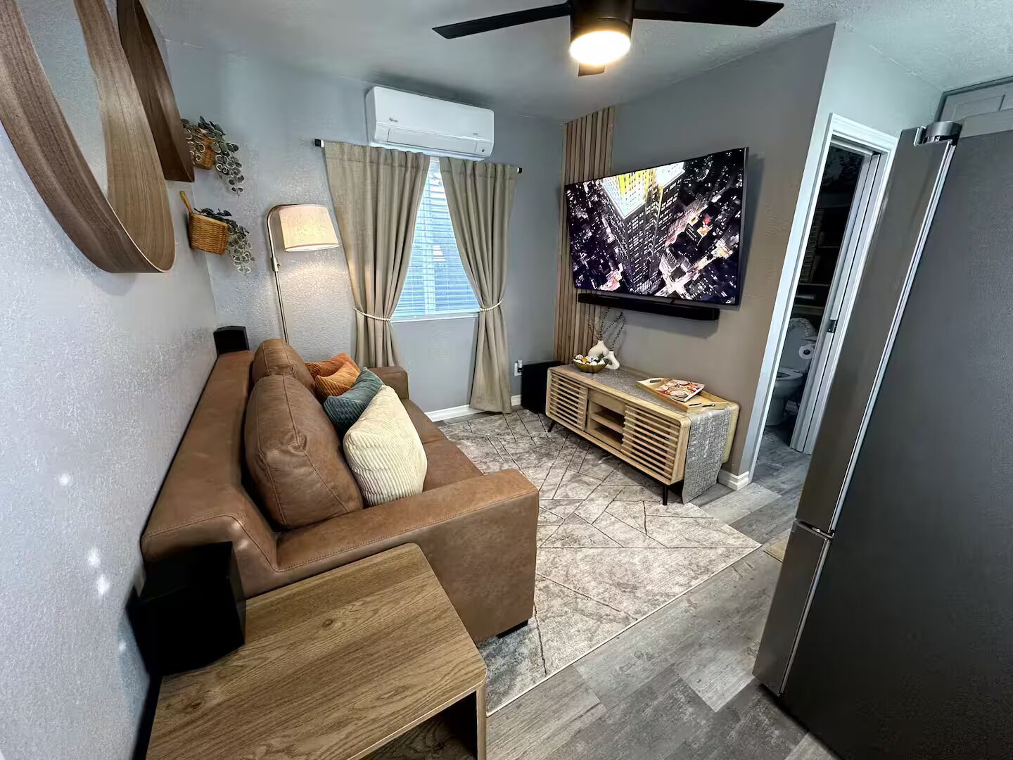 A living room with a brown sofa, a TV, a wooden console, and a ceiling fan.