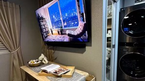 Un salon moderne doté d’un téléviseur à écran plat fixé au mur, d’un coin salon confortable et d’un appareil combiné lave-linge et sèche-linge encastré.
