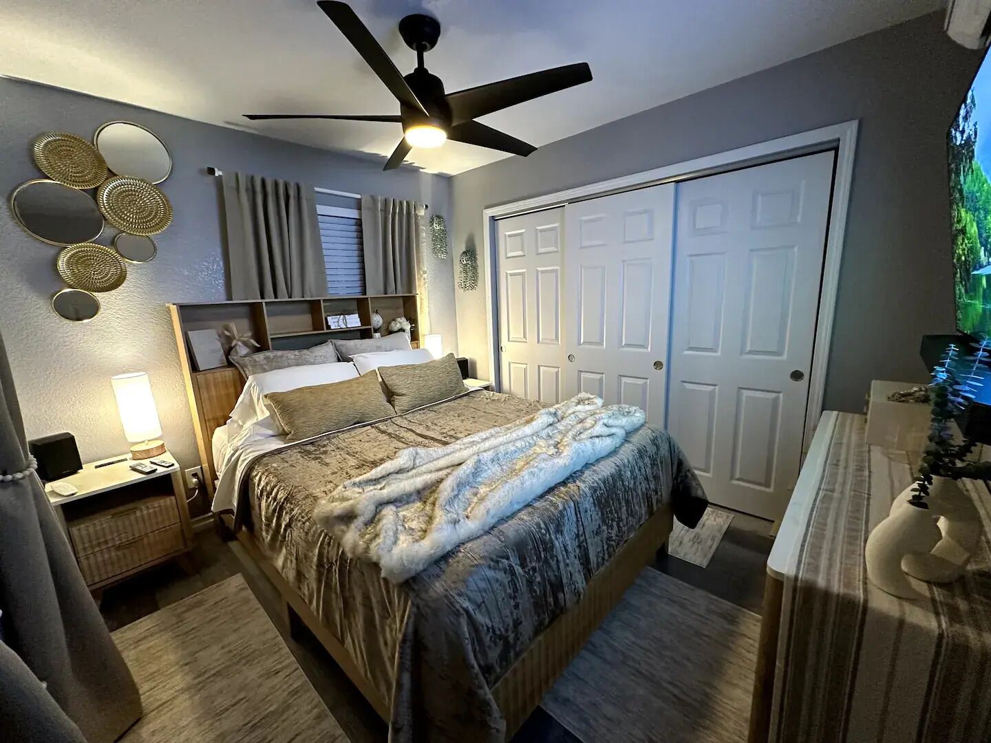 Un dormitorio con cama, mesitas de noche, ventilador de techo, armario y decoración en la pared.