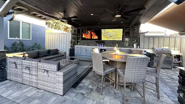 Une terrasse extérieure dotée d’une cheminée en pierre, de meubles en osier et d’un téléviseur fixé au mur.