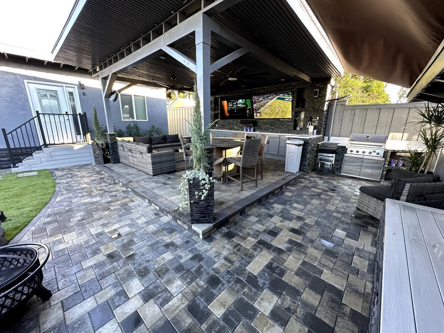 Eine Terrasse im Freien mit Steinboden, Grill, Fernseher und einer Sitzecke.