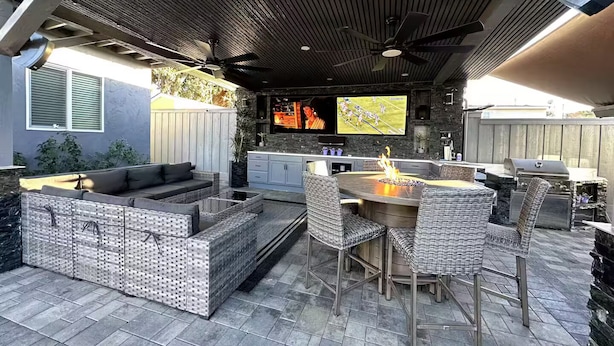 An outdoor patio with a stone fireplace, wicker furniture, and a television mounted on the wall.