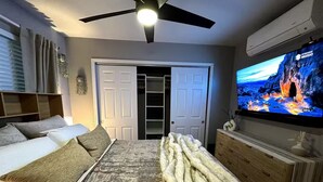 A bedroom with a bed, a TV, a ceiling fan, and a wardrobe.