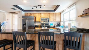 A modern kitchen with wooden cabinets, stainless steel appliances, and a central island with bar stools. - Coastal Coral Paradise with Heated Pool (Cape Coral)