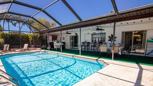 A swimming pool with a glass ceiling, surrounded by lounge chairs and a patio area with tables and chairs. - Coastal Coral Paradise with Heated Pool (Cape Coral)