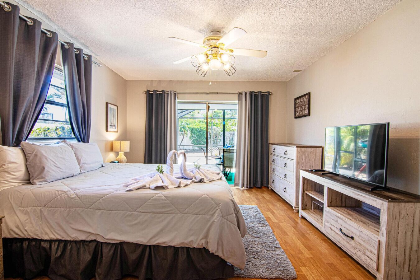 Ein Schlafzimmer mit Bett, Fernseher, Deckenventilator und Blick ins Freie.