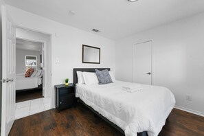 A bedroom with a bed, a nightstand, a mirror, and a door.