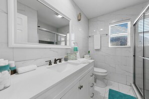 A modern bathroom with a white vanity, a large mirror, a toilet, and a glass shower enclosure.