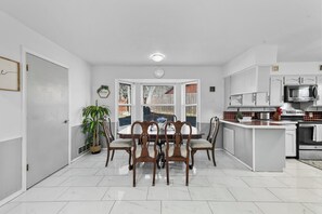 A modern kitchen with white cabinetry, a central island, and a dining area with a wooden table and chairs.