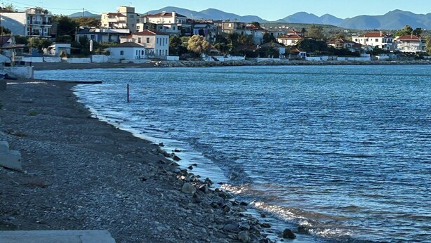Un poble costaner amb edificis al llarg de la riba, una platja rocosa i muntanyes al fons.