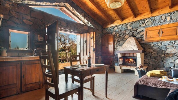 A rustic interior with a stone fireplace, wooden furniture, and a view of the outdoors. - House Finca Relax Cercadillo (Santa Ursula)