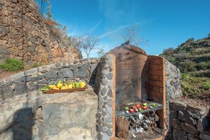 Una parrilla de piedra al aire libre con un muro de piedra y una bandeja de madera con verduras.