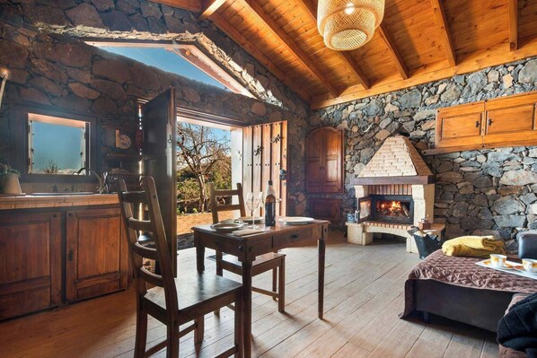 A rustic cabin interior with a stone fireplace, wooden furniture, and a dining area. - House Finca Relax Cercadillo (Santa Ursula)