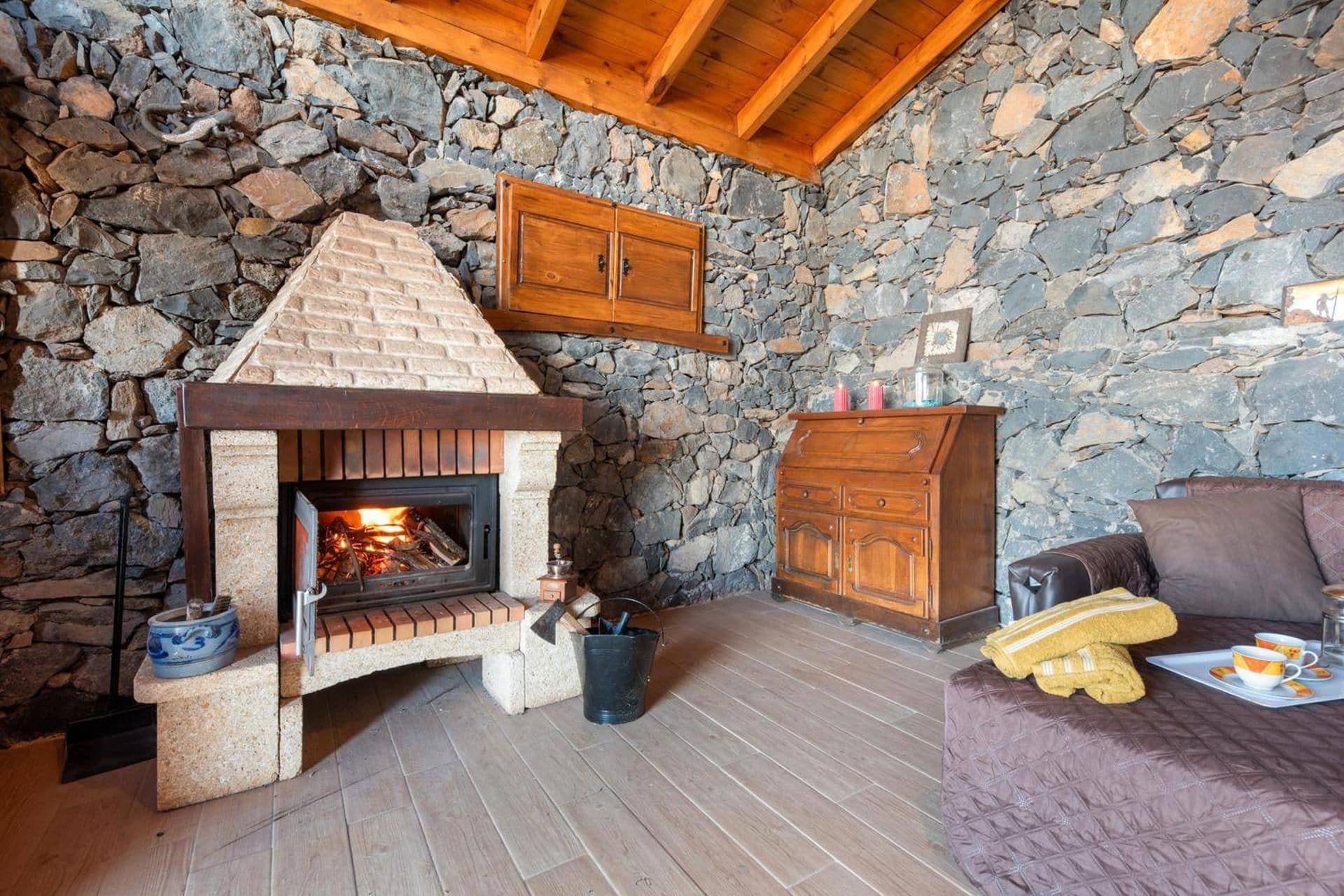 A stone fireplace with a wooden mantel, a stone wall, and a wooden ceiling.
