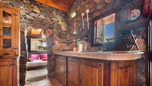A rustic kitchen with stone walls, wooden cabinets, and a cozy seating area with a pink pillow. - House Finca Relax Cercadillo (Santa Ursula)