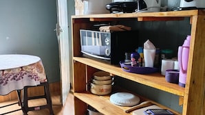 A kitchen with a wooden shelf holding a microwave, pots, and a water dispenser. - Wrech House 1989 - Sagana (Sagana)