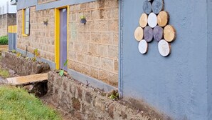 A building with a brick facade, a yellow door, and a wall decorated with circular wooden slices. - Wrech House 1989 - Sagana (Sagana)