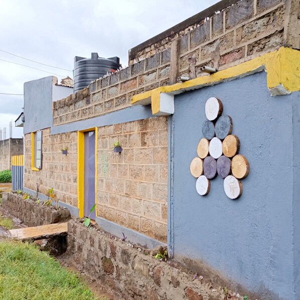 A building with a brick facade, a yellow door, and a wall decorated with circular wooden slices. - Wrech House 1989 - Sagana (Sagana)