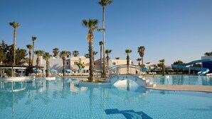 A large outdoor swimming pool with palm trees, a bridge, and a water slide. - Atlantica Marmari Beach (Kos)