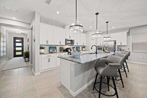 A modern kitchen with white cabinetry, a marble island, and two bar stools.