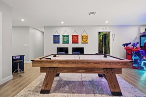 Una mesa de billar en una habitación con suelo de madera, televisor montado en la pared y una puerta con un mural de un bosque.