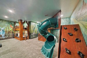 Une pièce décorée d’une fresque murale, équipée d’un toboggan et d’un mur d’escalade.