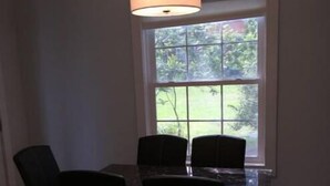 A dining area with a table and chairs, a hanging light fixture, and a window with a view of greenery.