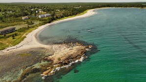 Vista aérea de una zona costera con una playa, un litoral rocoso y algunos edificios al fondo.