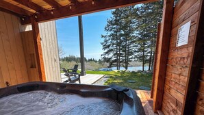 Un jacuzzi con cubierta de madera y vista a un lago y árboles.