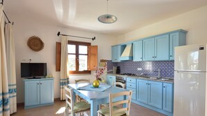 A compact kitchen with blue cabinets, a white refrigerator, and a dining area with a table and chairs. - Villa Menhir! (Sardegna)