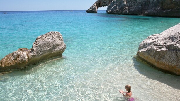 A clear turquoise sea with rocky formations and a person in the water. - Villa Menhir! (Sardegna)
