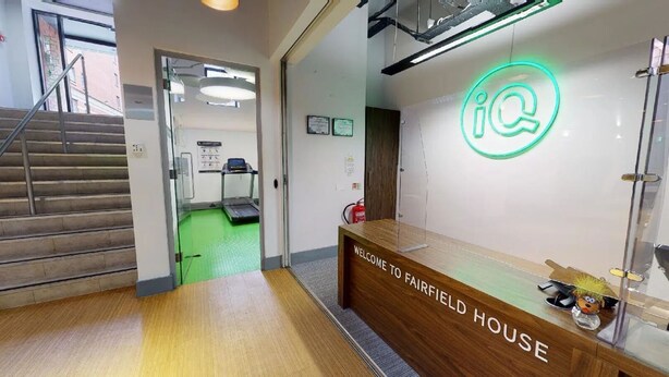 A reception desk with a sign reading "WELCOME TO FAIRFIELD HOUSE" and a neon sign with a question mark.