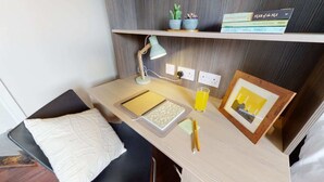 A small, neatly organized workspace with a desk, a lamp, a notebook, a glass of juice, and a framed picture.