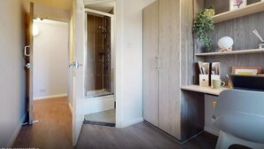 A modern bathroom with a shower, wooden cabinets, and a desk area with a chair and shelves.