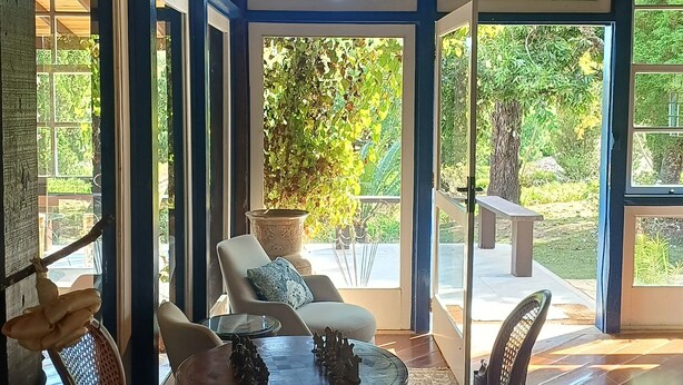 Un intérieur en bois avec une table ronde et des chaises, de grandes fenêtres et une vue sur la verdure à l’extérieur.
