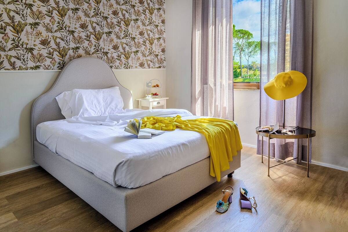 Une chambre à coucher avec un lit, une table de chevet, une lampe et une vue sur l’extérieur.