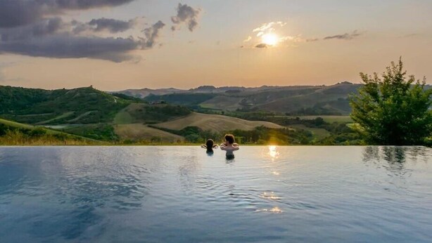 Una piscina infinita con vistas a colinas ondulantes y una puesta de sol.