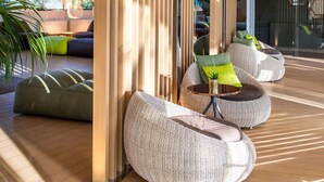 Un espacio interior moderno con suelo de madera, zona de estar con sillas redondas de fibra natural y un alto panel divisor de madera.