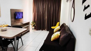 A modern living room with a wooden dining table, a sofa with cushions, a TV on the wall, and a large window with curtains. - Hotel Riviera Caldas Novas, in the city center. Pet friendly, (Turista 1 Caldas Novas)
