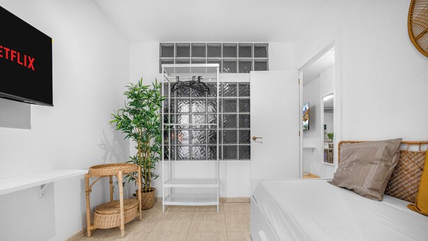 Een moderne slaapkamer met een bed, een aan de muur bevestigde televisie, een raam met uitzicht en een deur naar een andere kamer.