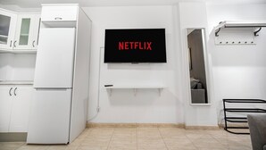 A modern kitchen with white cabinetry, a built-in refrigerator, a wall-mounted TV displaying "NETFLIX," and a small shelf below the TV.