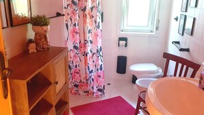 Een badkamer met een houten wastafelmeubel, een witte wasbak, een toilet en een douchegordijn met een bloemenprint.