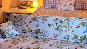 Een bed met bloemenbedekking, een bedlampje en een plank met ingekaderde foto's.