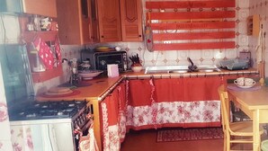 Een praktische keuken met houten kastjes, een gasfornuis, een spoelbak en een klein zite hoekje met een tafel en stoelen.