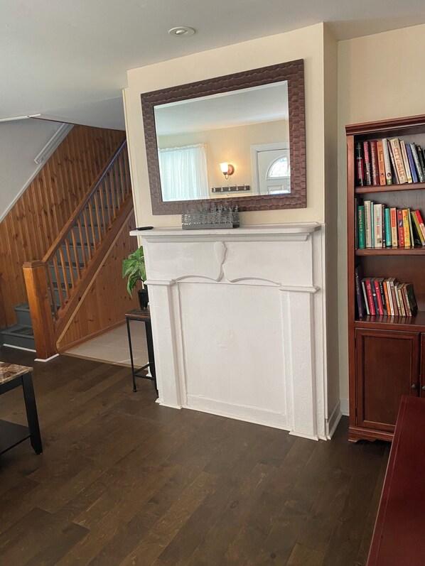 A living room with a white fireplace, a wooden staircase, and a bookshelf. - Lovely 2 Bedroom Unit in Long Branch, close to the beach, and NJ Transit. (Long Branch)