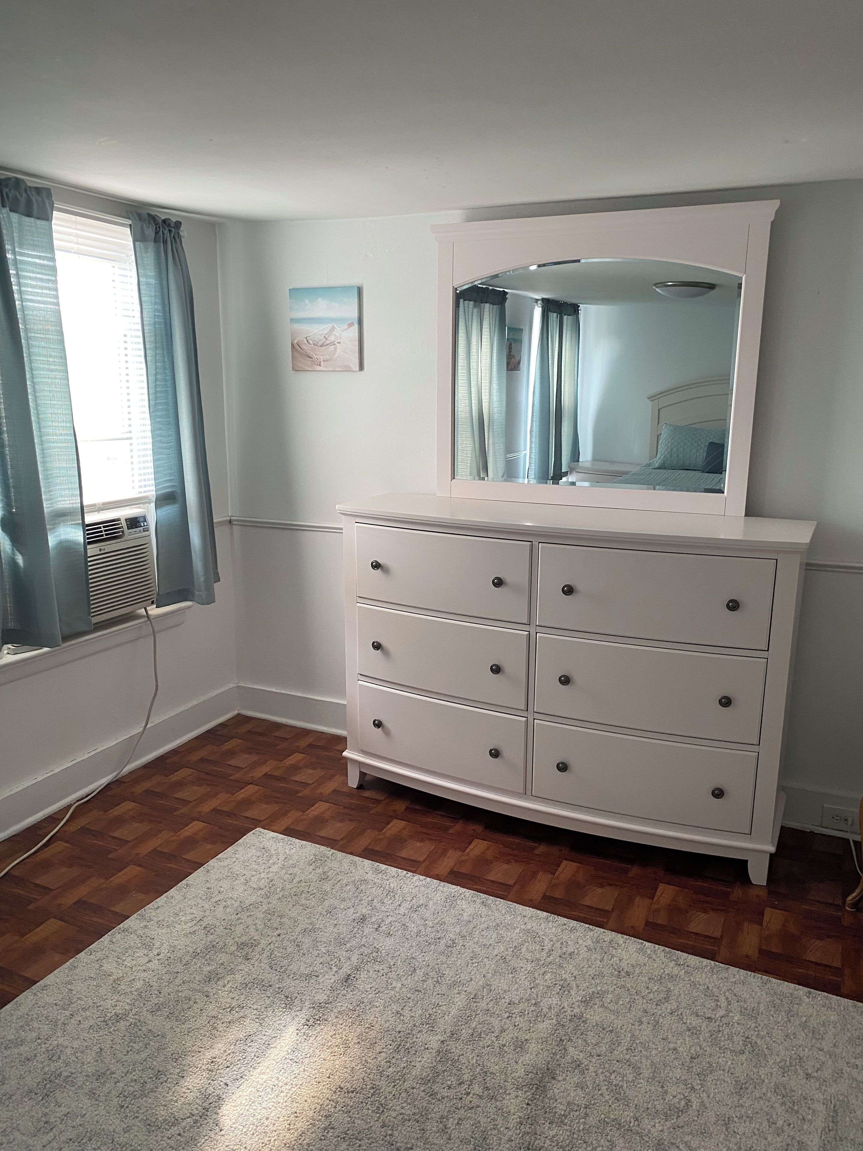 A room with a white dresser, a mirror, and a window with curtains.