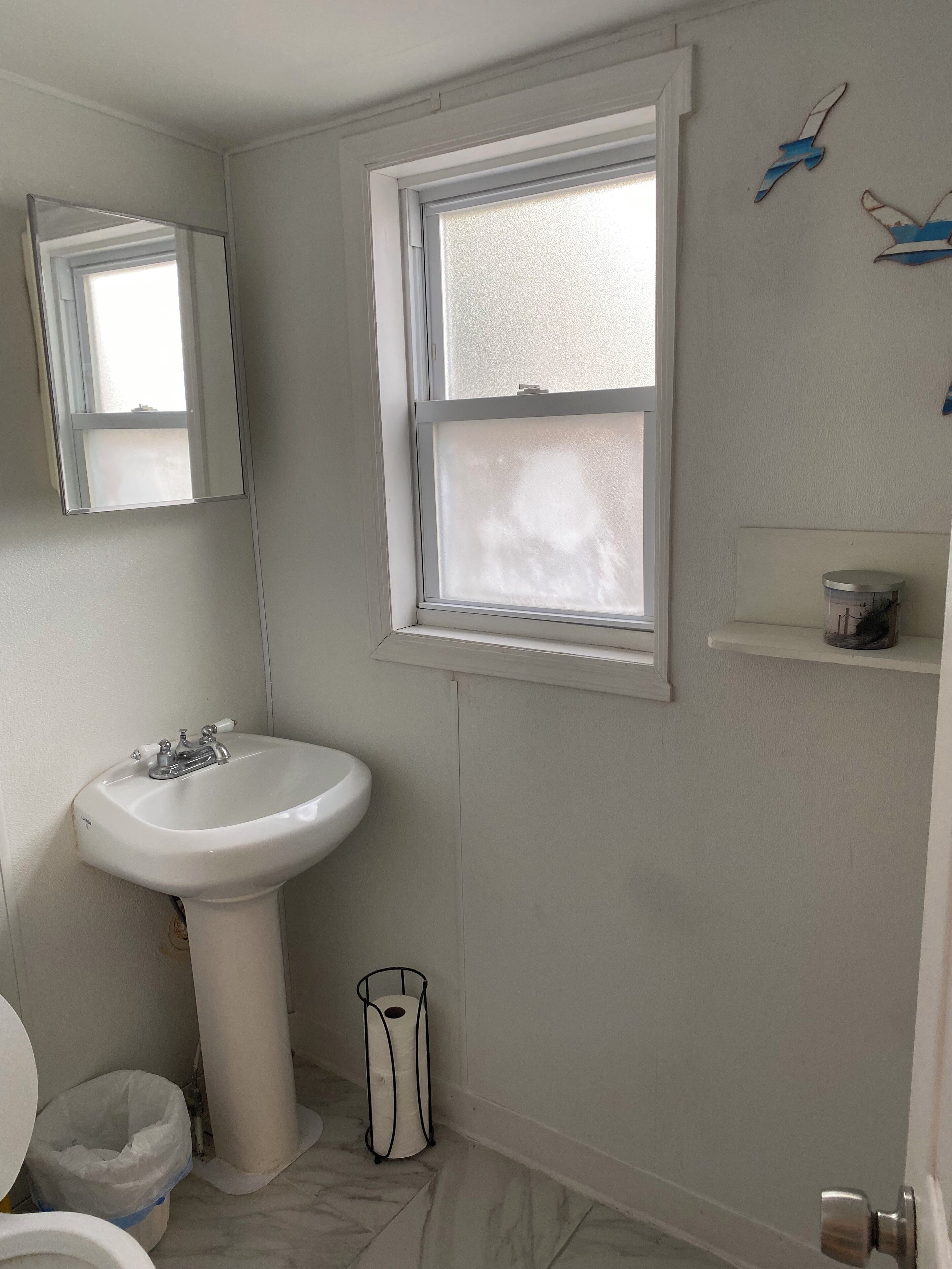 A bathroom with a white sink, a mirror, a window, and a toilet.