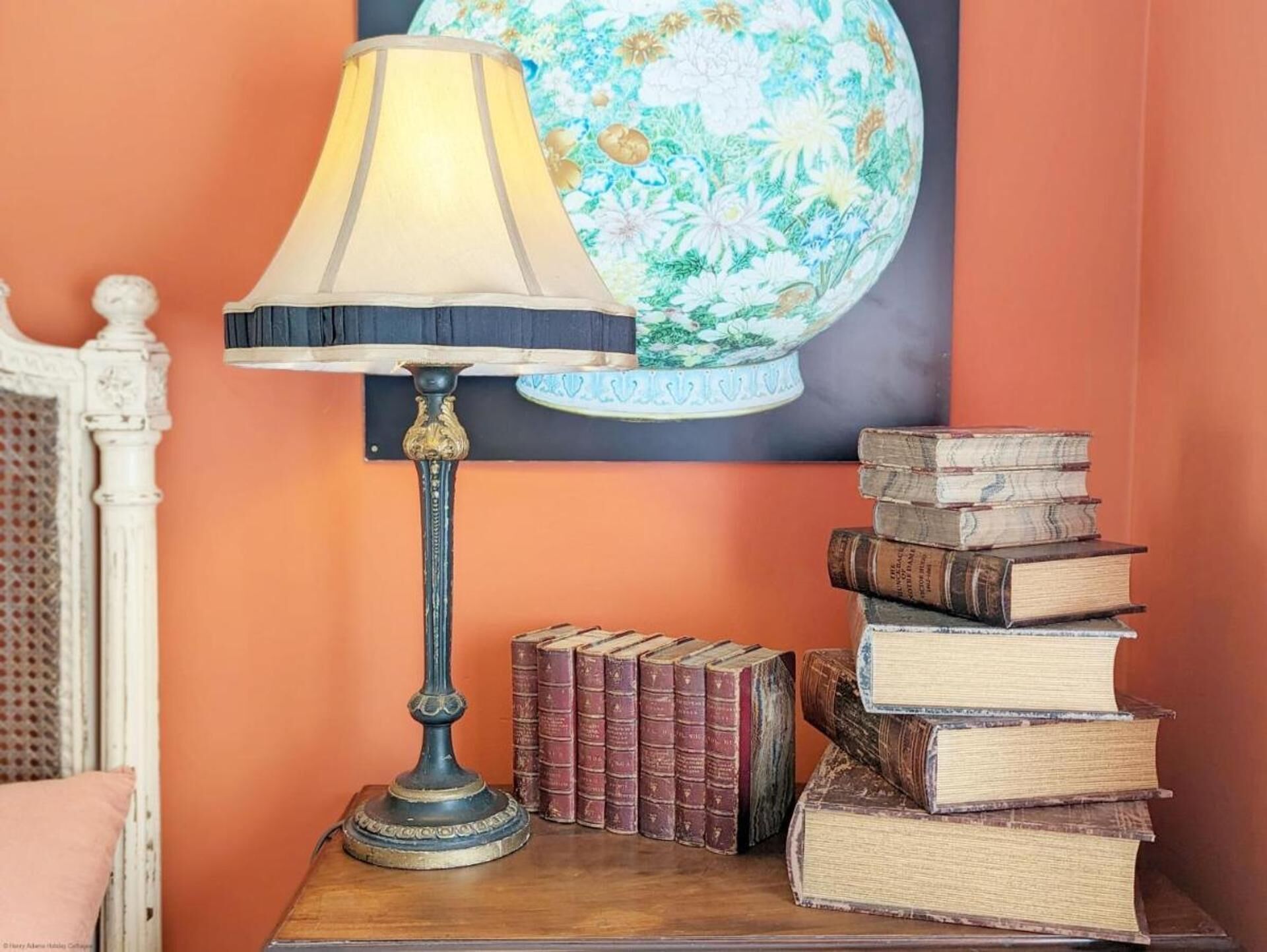 A table with a lamp and a stack of books against a wall with a floral globe.